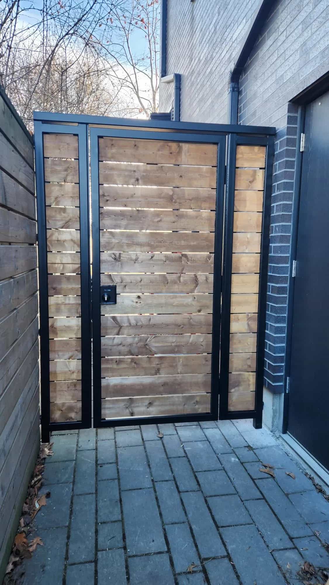 Black steel-framed walk-through gate with horizontal natural wood boards closing a narrow side passage