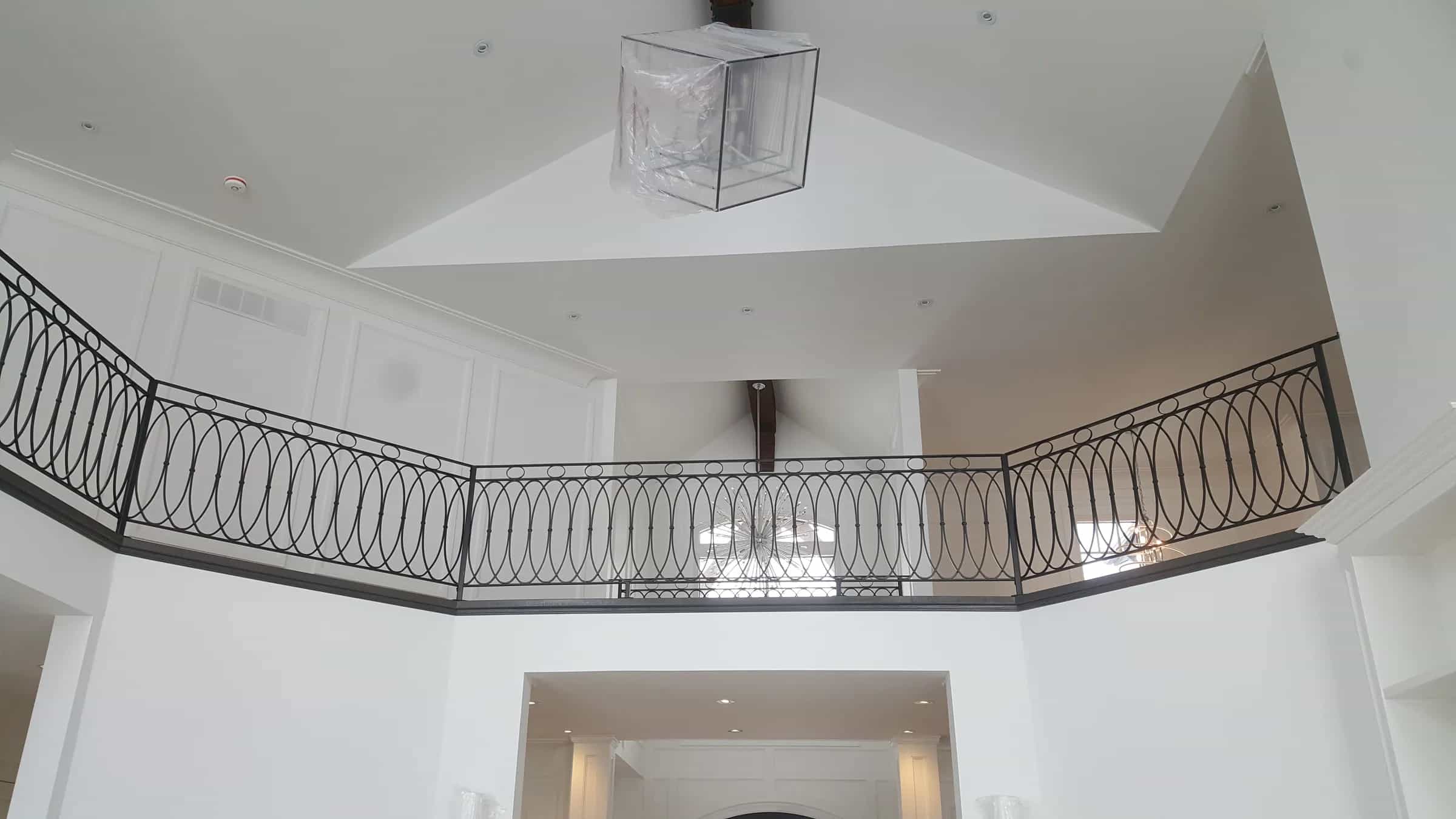 Black wrought iron railing with interlocking oval loops along a curved loft edge above a white two-storey foyer