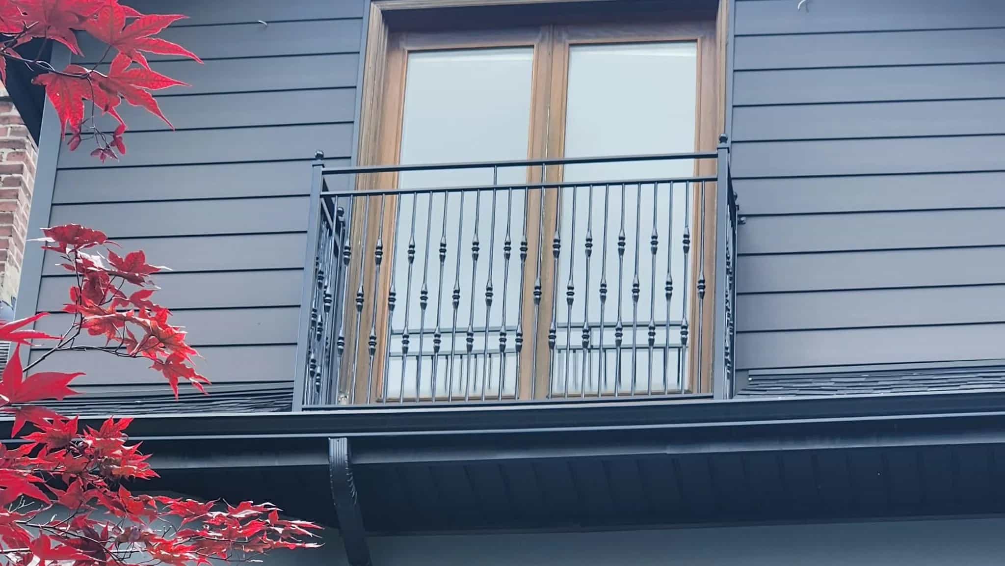 Black metal Juliet railing with decorative collared balusters across wood-framed French doors on dark grey siding