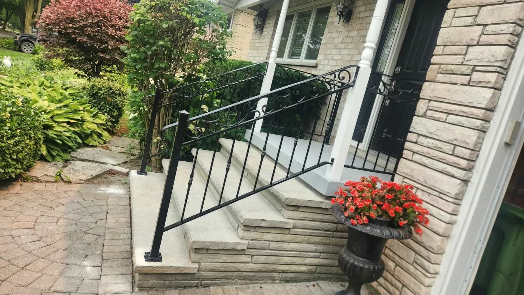 Black ornamental iron railing with a scrolled top rail running down light stone front steps beside a white porch column