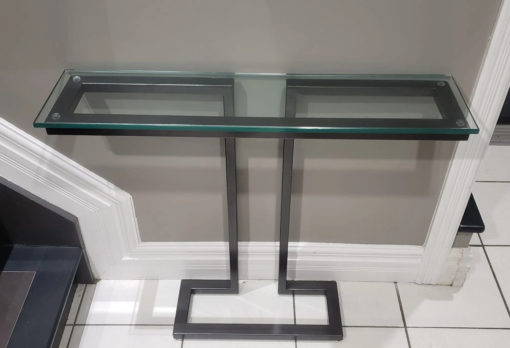 Console table with a clear glass top on two black steel uprights joined by a rectangular floor base