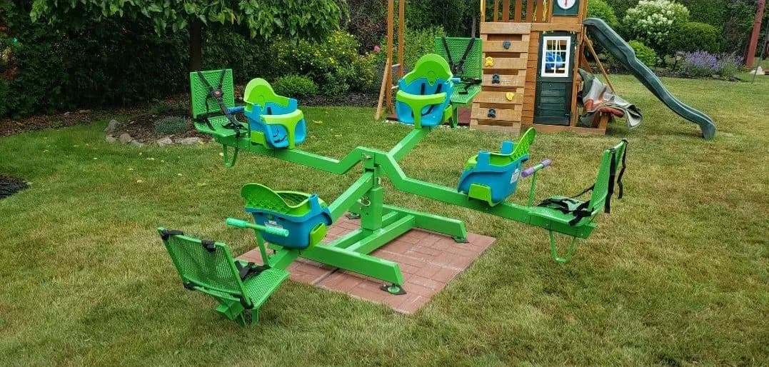 Bright green metal play set with arms carrying child bucket seats and bench seats, installed on a brick pad on a lawn