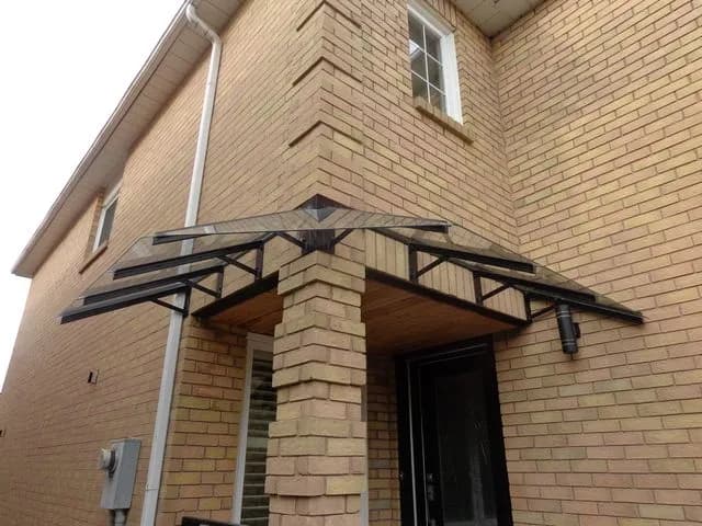 Glass canopy on a black steel frame with angled supports above a front entrance and brick column