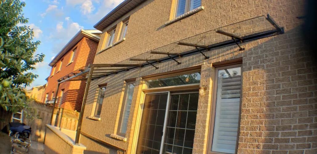 Clear glass canopy on black steel brackets running across patio doors on the back of a brick house