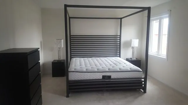 Black steel four-poster canopy bed frame with a horizontal-slat headboard in a bright bedroom