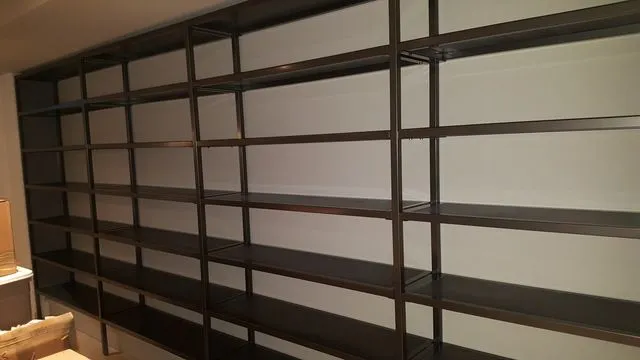 Long dark steel shelving frame with many open bays spanning a living room wall