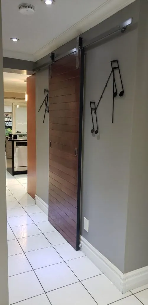 Wood sliding barn door hung on a black steel track in a hallway, next to black steel music-note wall art