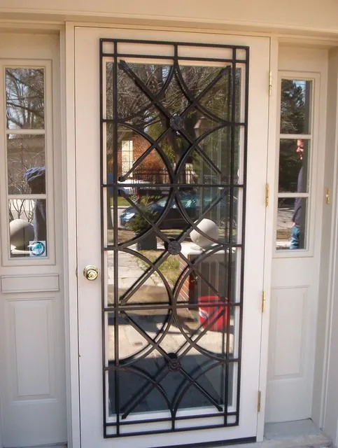 Black steel grille with pointed arches and quatrefoils fixed over the glass of a white front door with sidelights