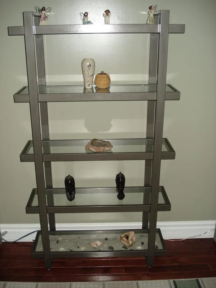 Freestanding shelving unit with a brushed steel frame and five glass shelves holding small ornaments