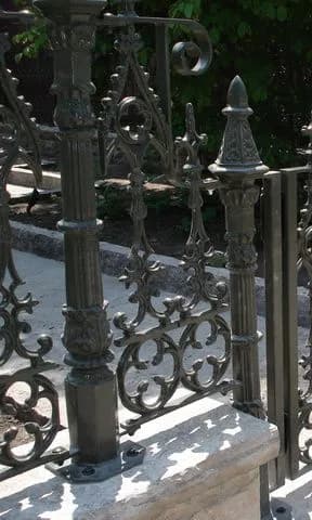 Bronze-green ornamental fence with Gothic spire posts and pierced scroll panels mounted on a low stone wall