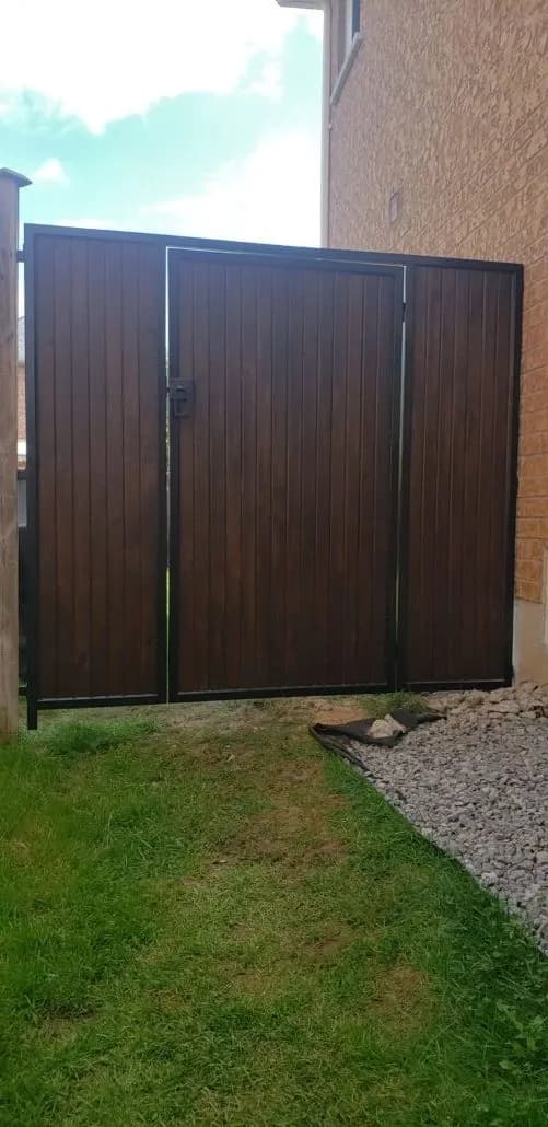 Black steel-framed gate with dark vertical wood infill closing a side yard beside a brick house