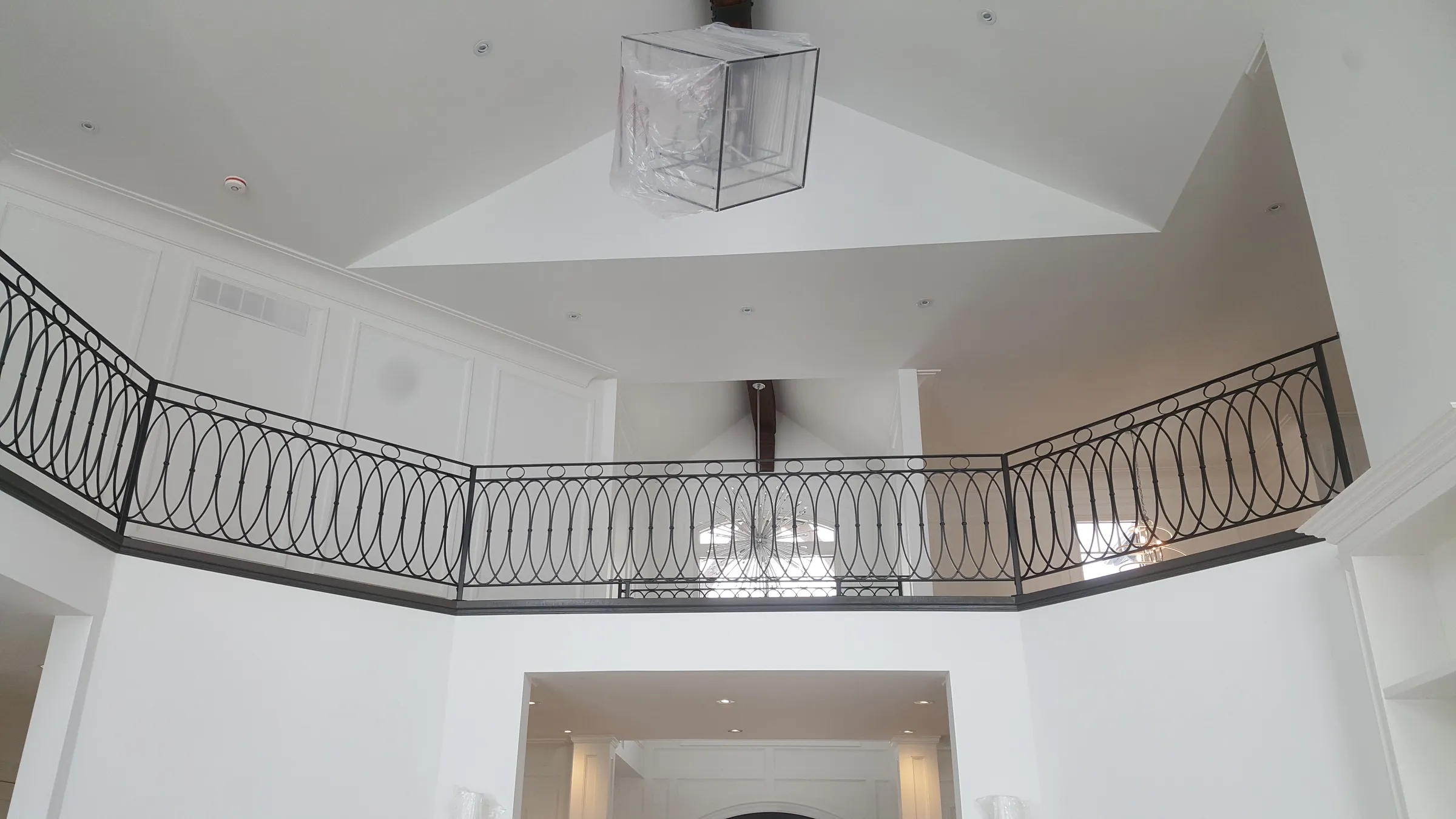 Black wrought iron railing with interlocking oval loops along a curved loft edge above a white two-storey foyer