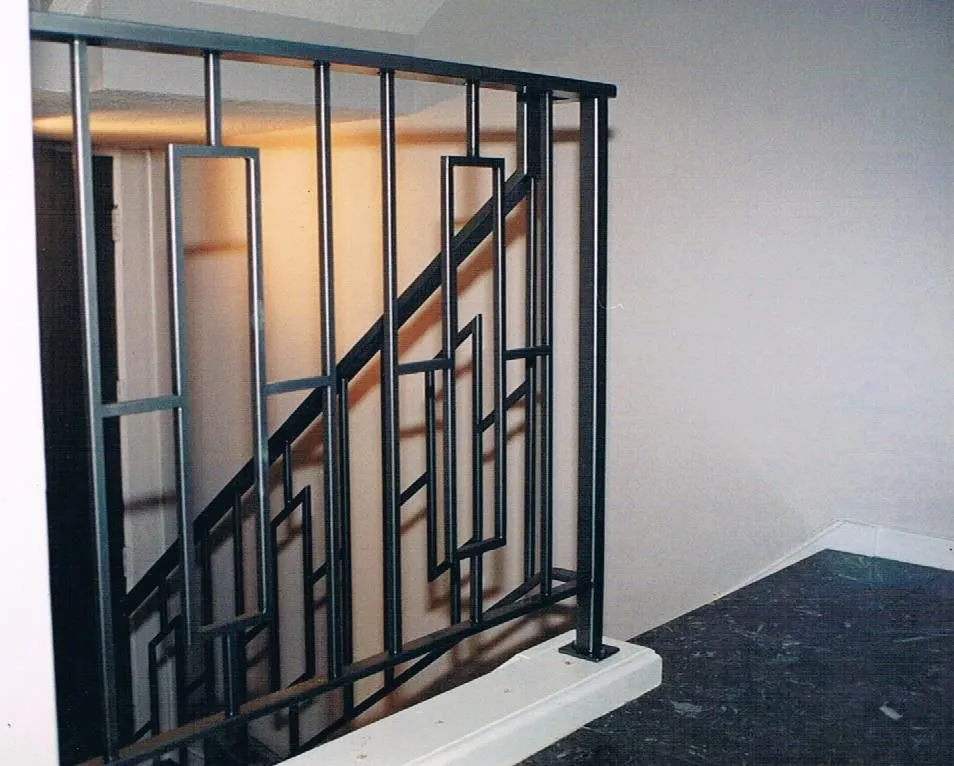 Black steel railing whose balusters form nested, offset rectangles in an Art Deco pattern beside a staircase