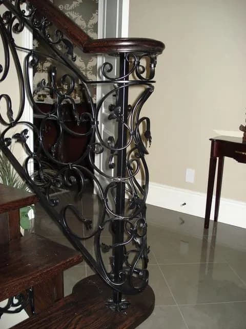 Heavily scrolled black wrought iron panels and a wrapped iron newel at the foot of a curved wood staircase