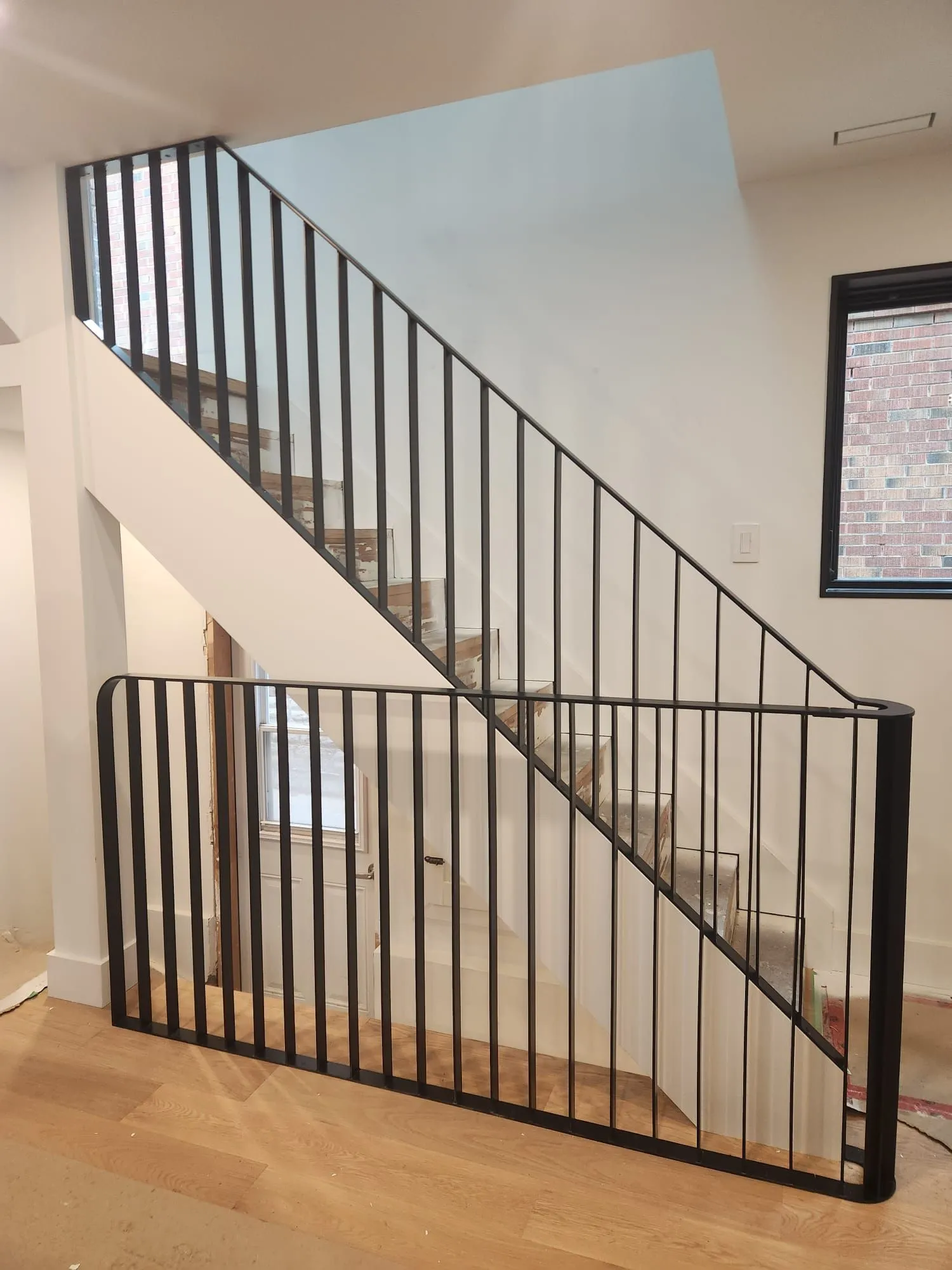 Black steel stair railing with slim vertical pickets on a straight staircase, with a matching guard at the bottom landing