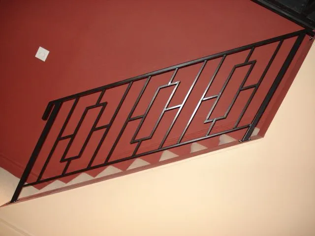 Black steel stair railing with an interlocking stepped geometric pattern along a staircase beside a deep red wall