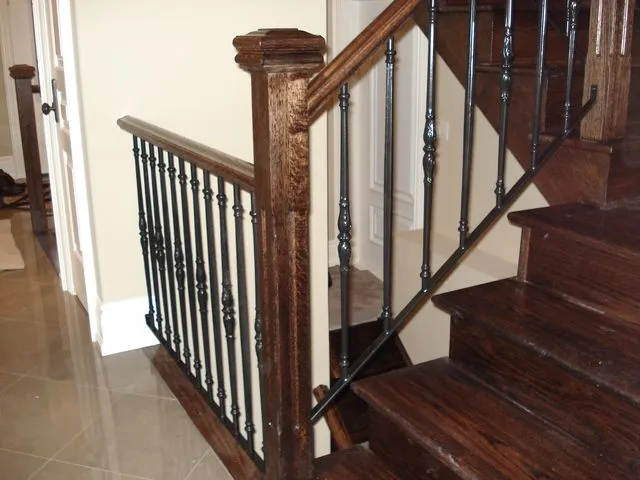 Black wrought iron balusters with decorative collars between a dark wood handrail and newel on a hardwood staircase