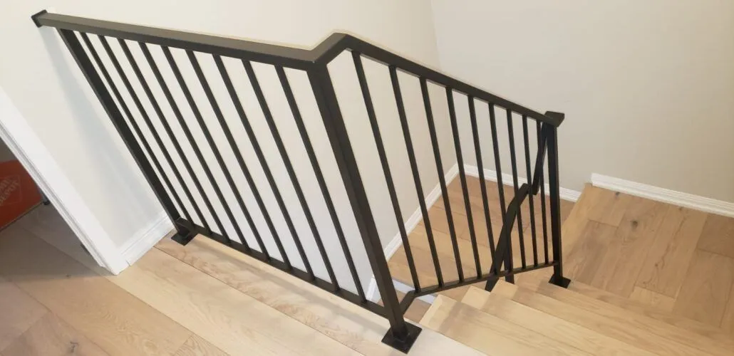 Minimal black steel railing with straight pickets turning a corner at the top of a staircase on light oak flooring