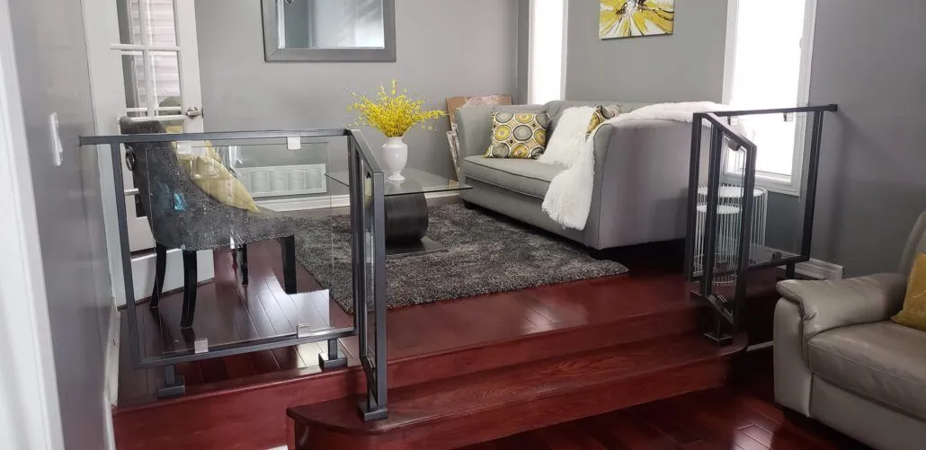 Short clear glass railing with black posts beside two hardwood steps leading down into a sunken living room
