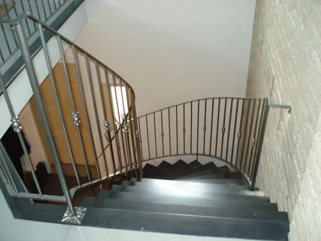 Charcoal steel railing with decorative collars curving down a winding staircase with dark treads beside a brick wall