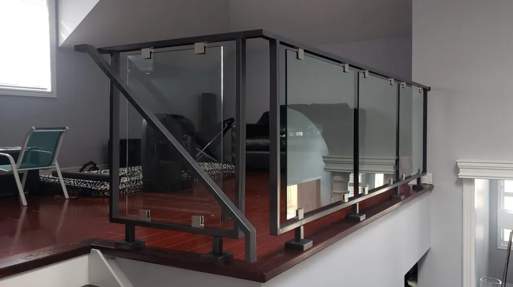 Clear glass panels between black square steel posts and a flat black handrail along a raised landing with red hardwood