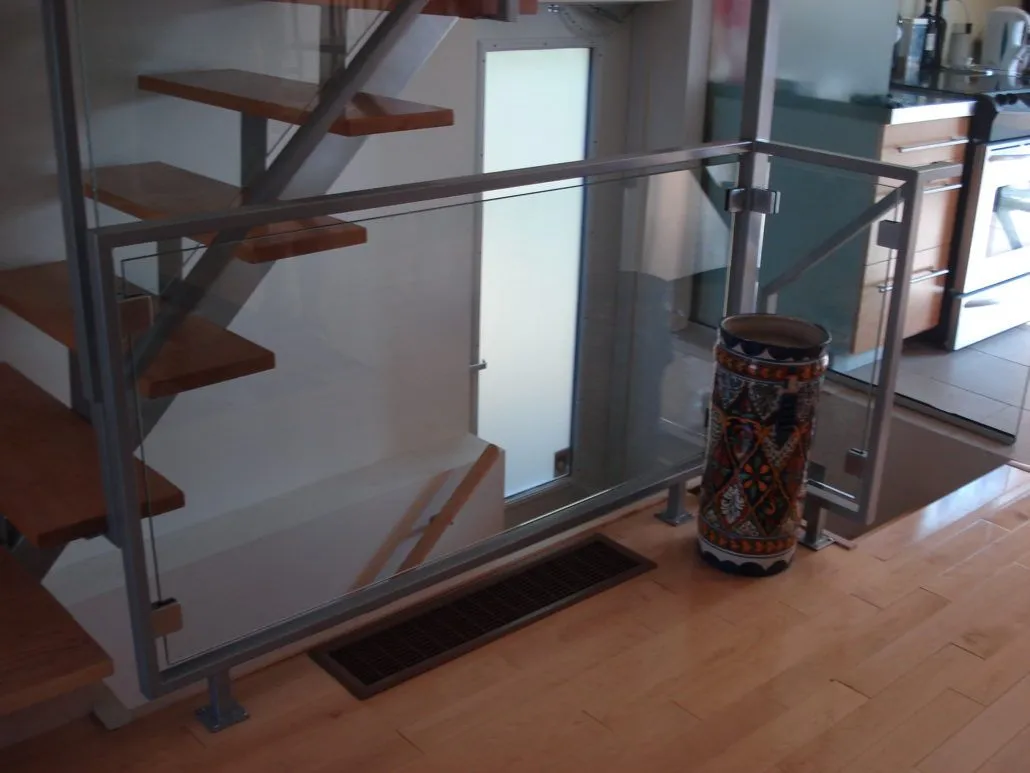 Glass panels with brushed stainless posts guarding the side of an open staircase with floating wood treads