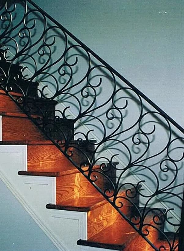 Black wrought iron railing filled with continuous S-scrolls along the side of a staircase with warm wood treads