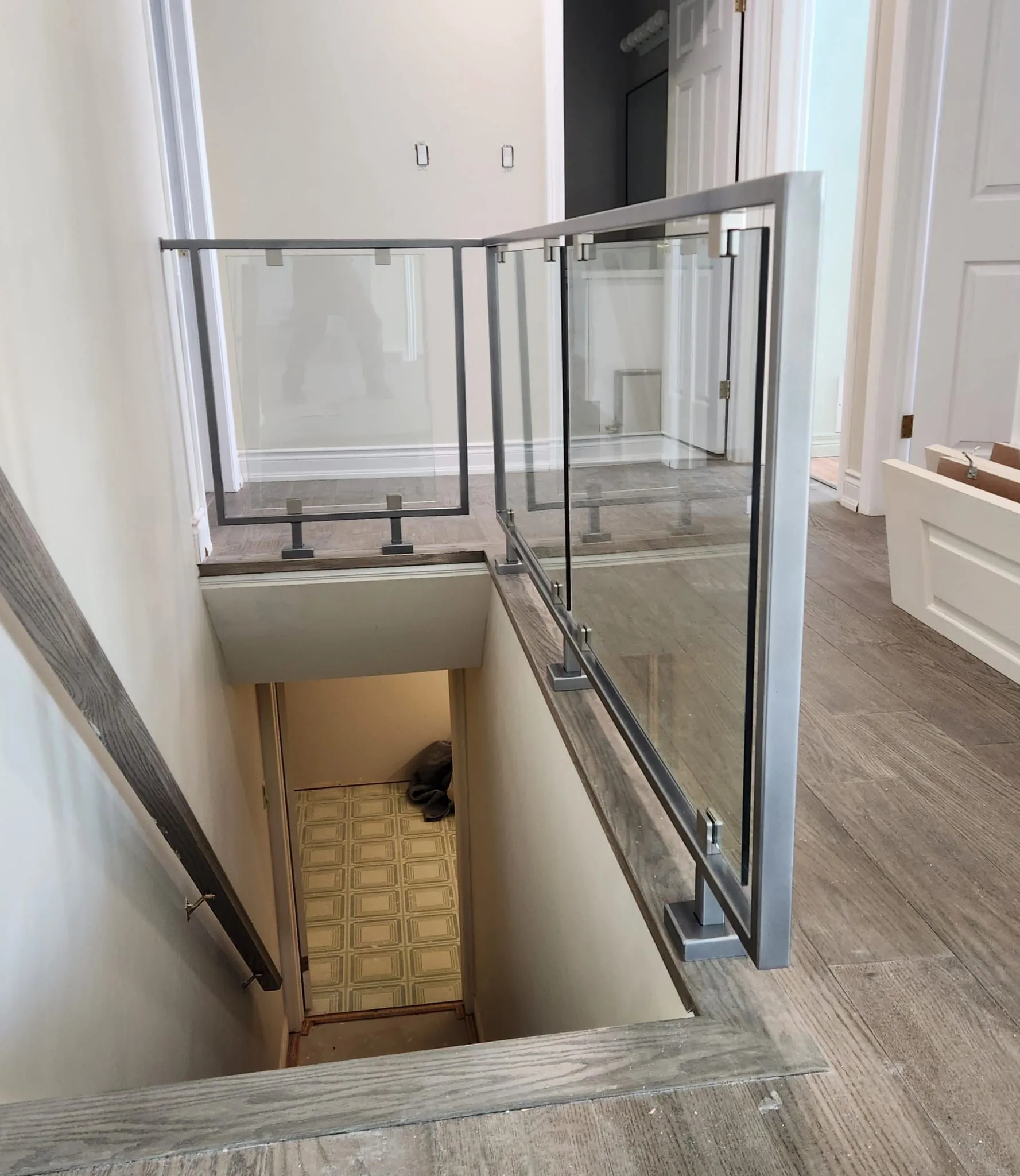 Clear glass panels with stainless steel posts and handrail around a basement stair opening on a grey wood-look floor