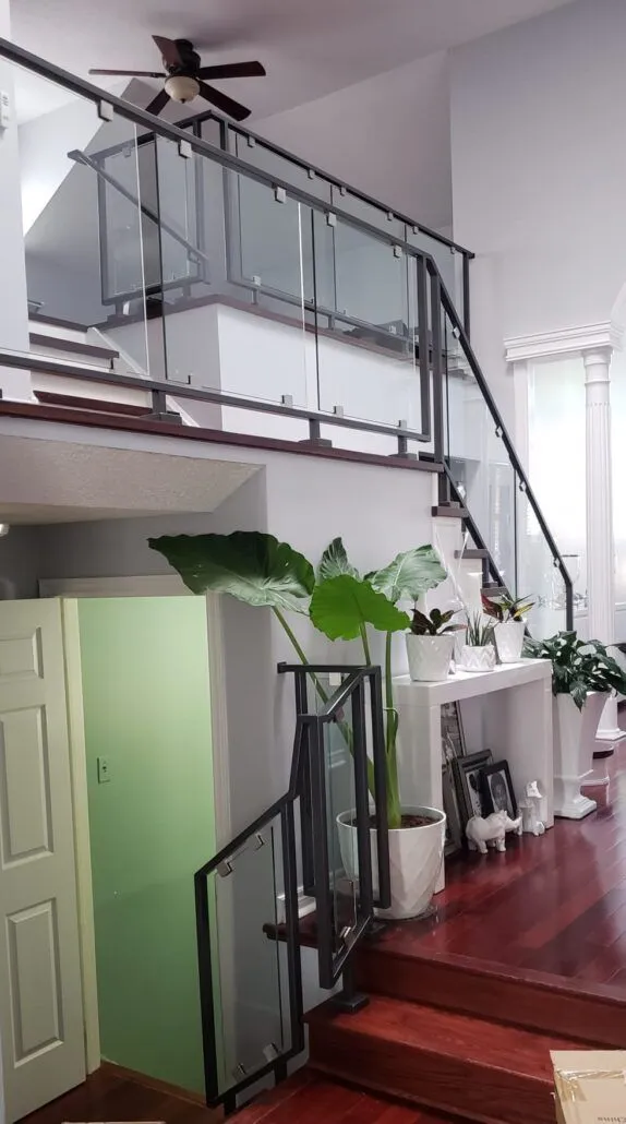 Glass panels held by black posts and clamps along a split-level staircase and the loft above it