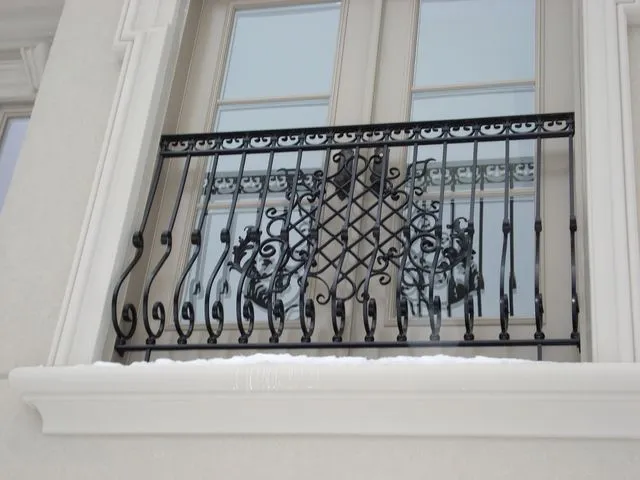 Black wrought iron Juliet railing with a scroll and lattice centre panel across French windows, snow on the sill