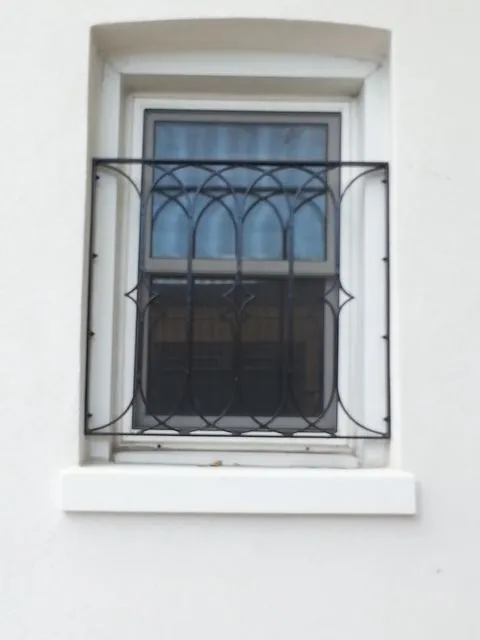 Black iron window guard with arched top bars and a bowed front fixed across a single window in white stucco
