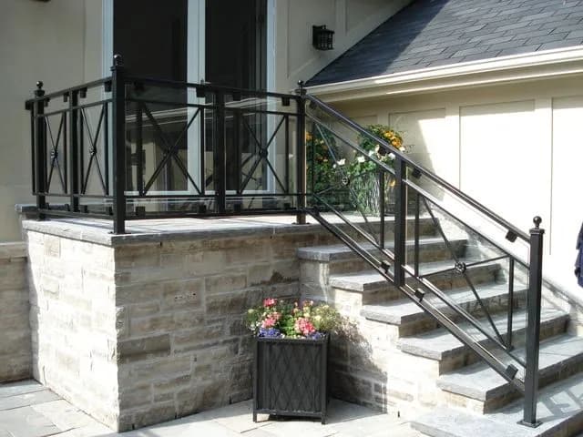 Black steel porch guard and step railing with X-pattern panels and ball-top posts on a light stone porch