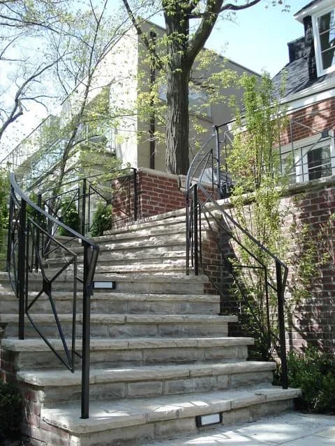 Black steel railings with a diamond-pattern panel on both sides of a long flight of stone steps up to a house