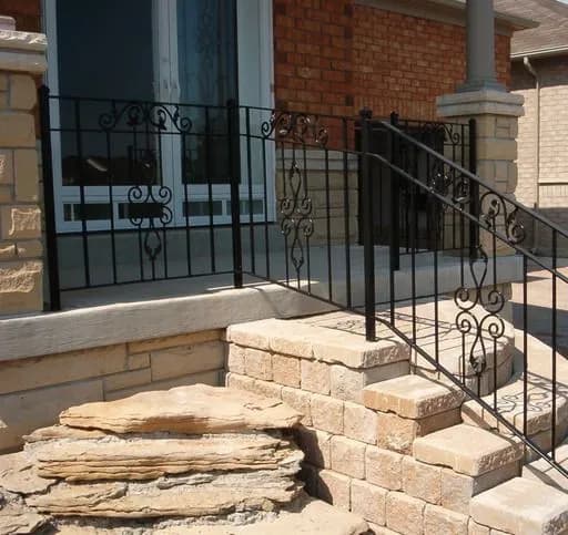 Black iron porch railing with scroll inserts and a step railing following curved interlocking stone steps