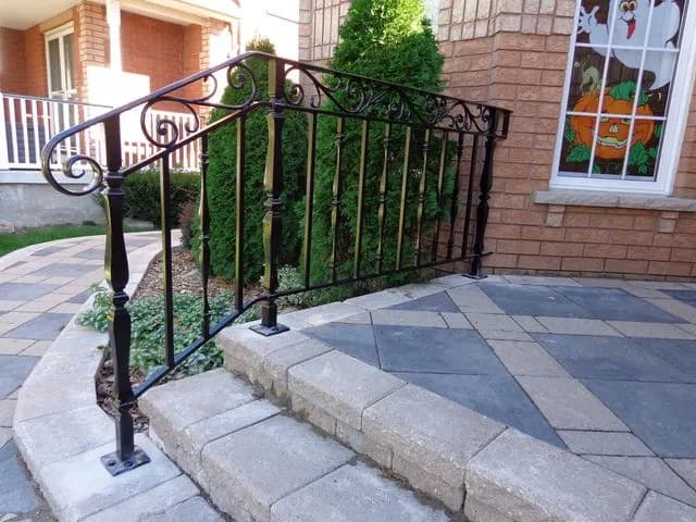 Black iron step railing with a scrolled top rail and turned newel post on curved interlocking stone steps