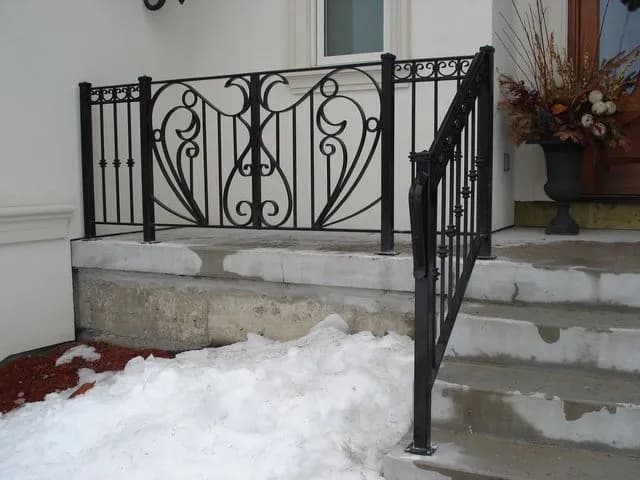 Black wrought iron porch railing with heart-shaped scroll panels and a matching railing down concrete front steps