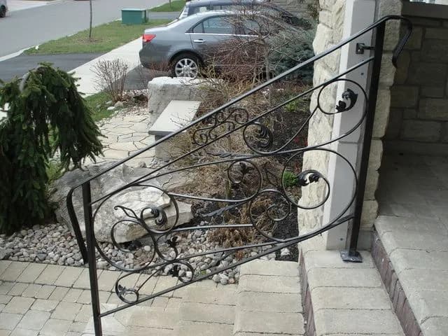 Black wrought iron railing with loose scroll infill running down the side of natural stone front steps