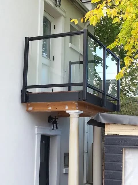 Black-framed glass railing around a small upper-floor balcony built over a front porch with white columns