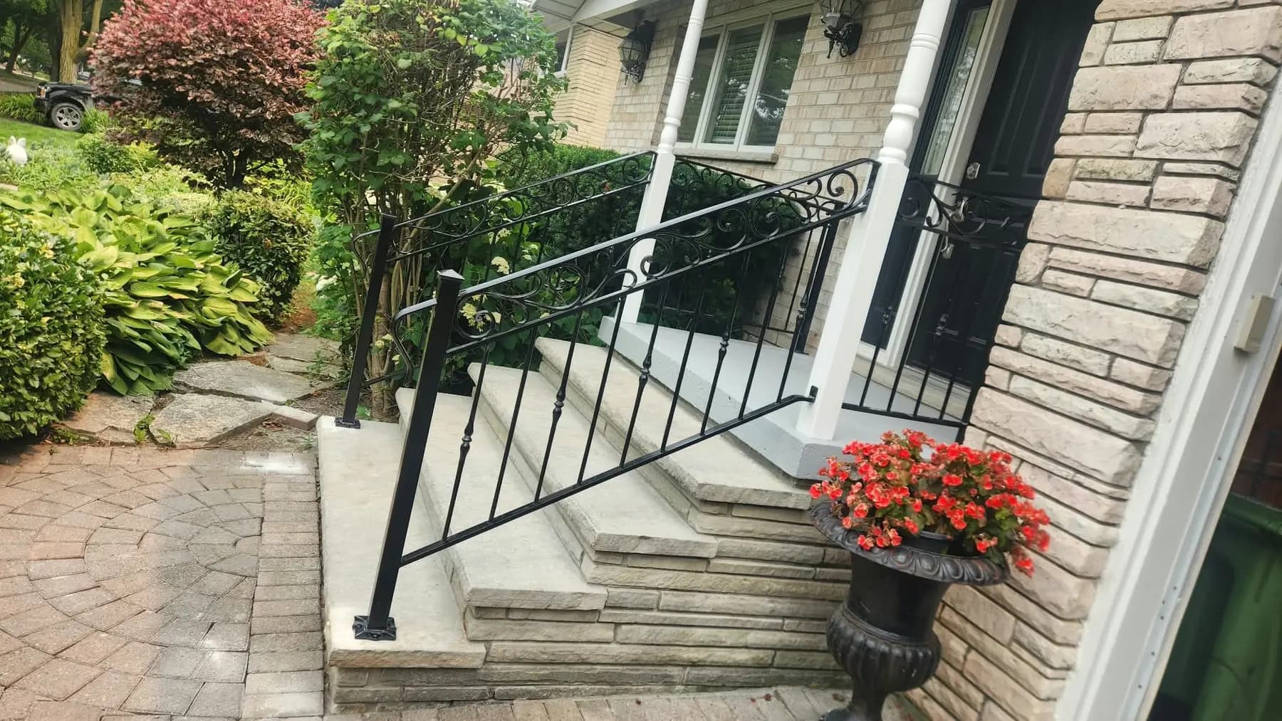 Black ornamental iron railing with a scrolled top rail running down light stone front steps beside a white porch column