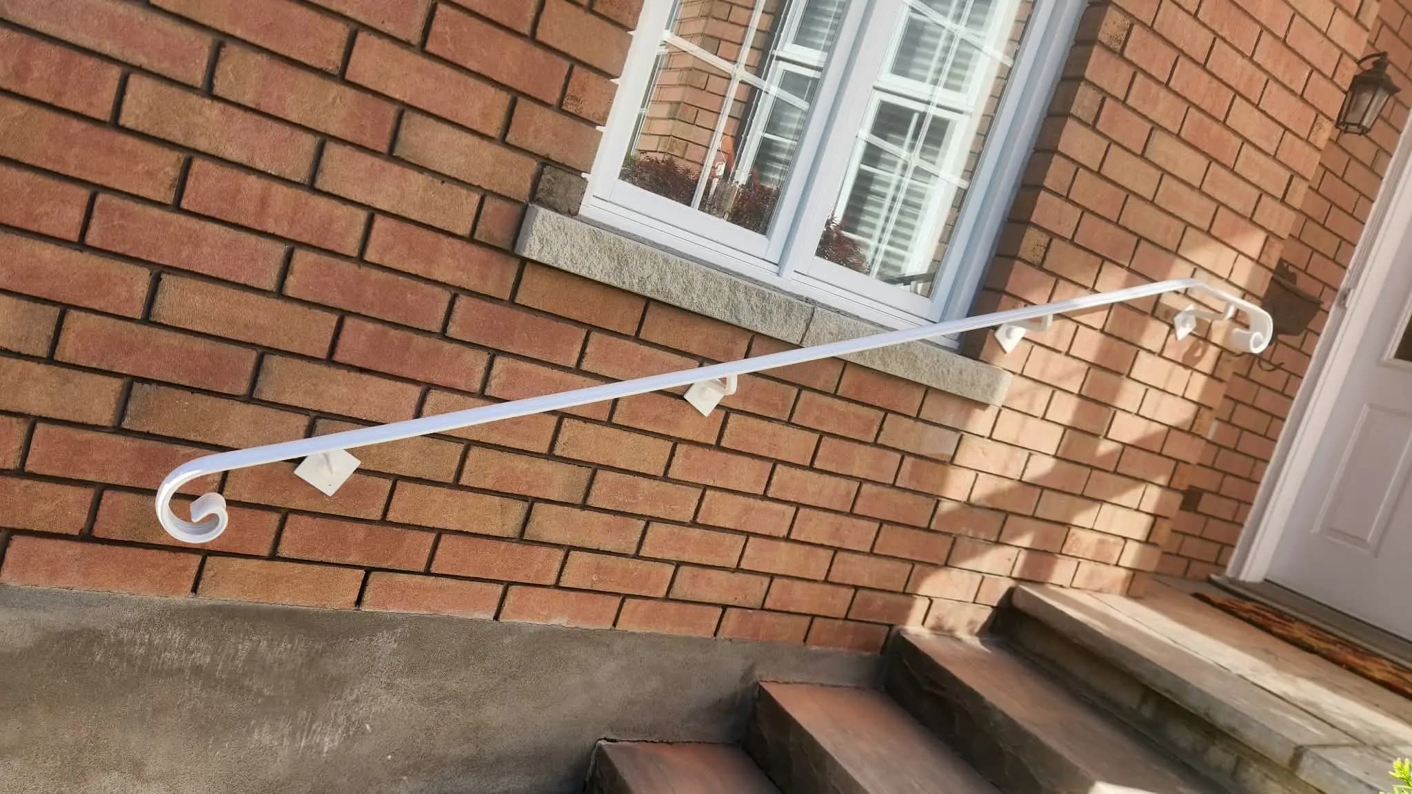White metal handrail with curled scroll ends mounted on a red brick wall beside a short flight of front steps