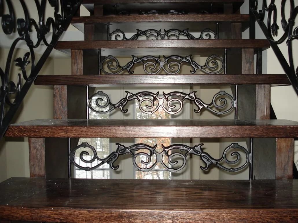 Dark wood stair treads with black wrought iron scroll panels in the risers and ornate scroll railings on each side