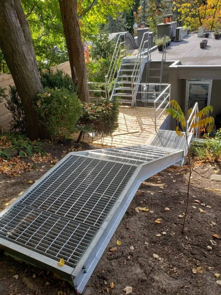 Galvanized steel grating walkway crossing a garden to galvanized stairs and railings that climb to a rooftop deck