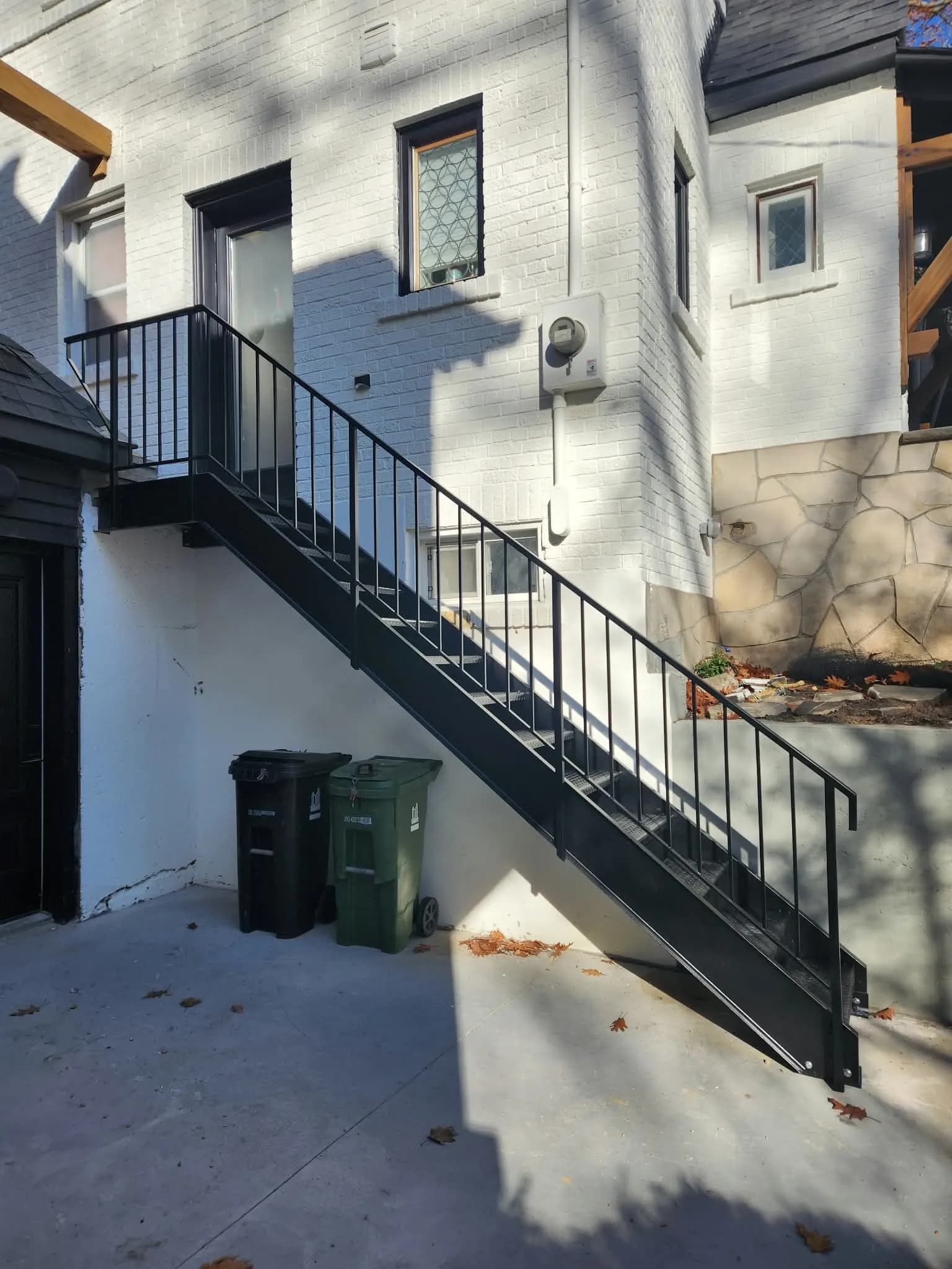 Straight black metal exterior staircase with a picket railing rising along a white brick wall to a side door